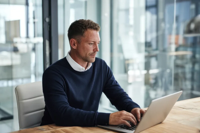 Man working on laptop at wooden desk in modern office