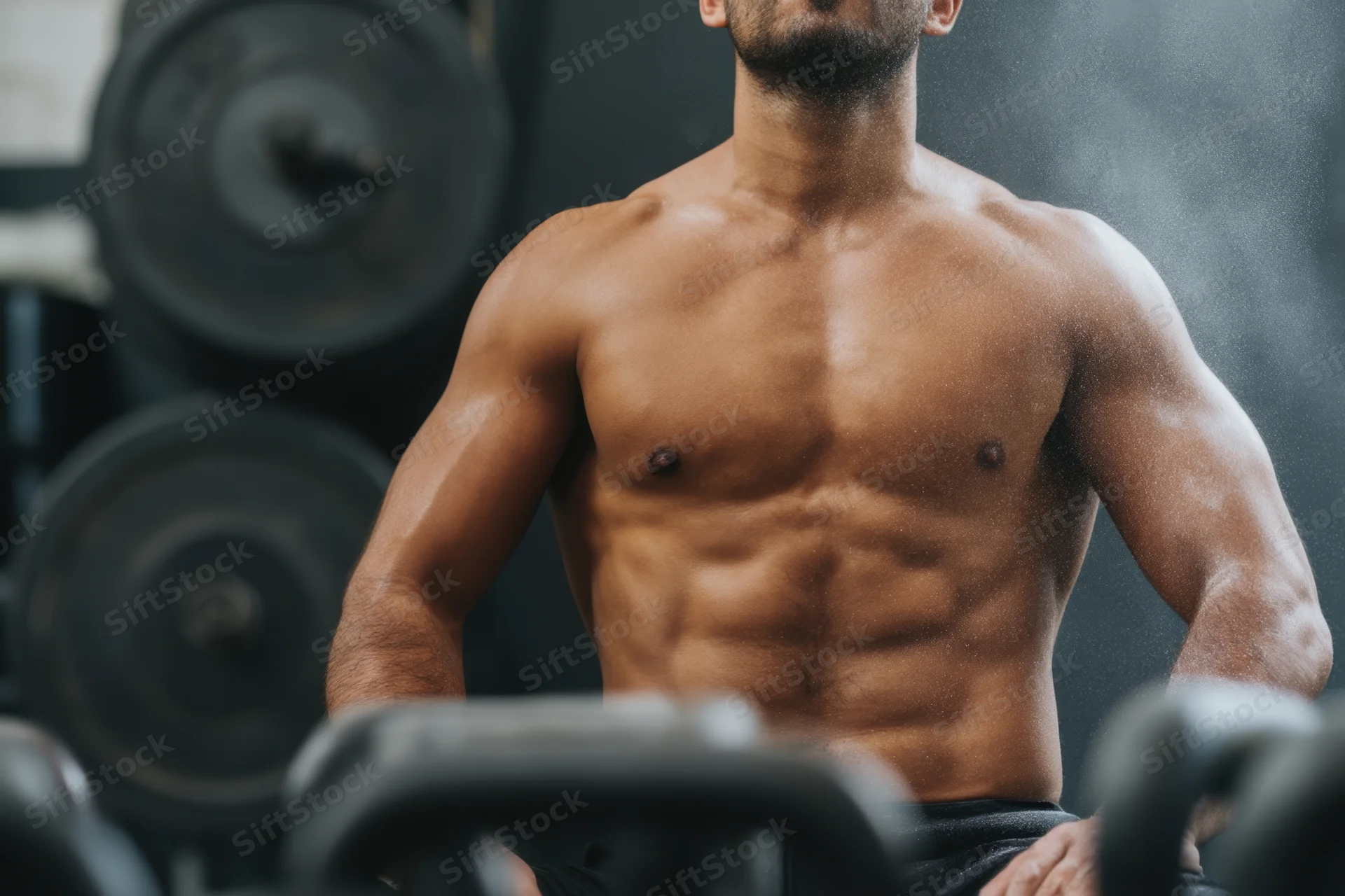 Muscular man with defined abs and arms in a gym, surrounded by weights and chalk dust swirling in the air
