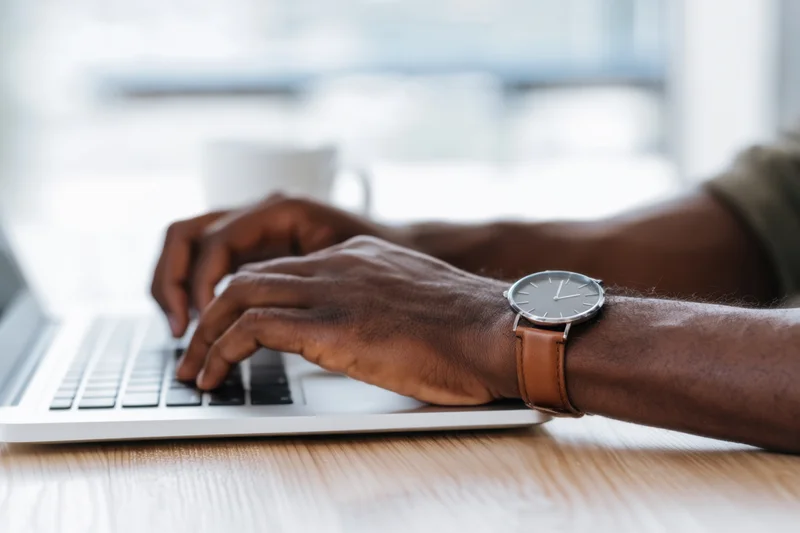 Hands typing on a silver laptop at a wooden desk in an office setting