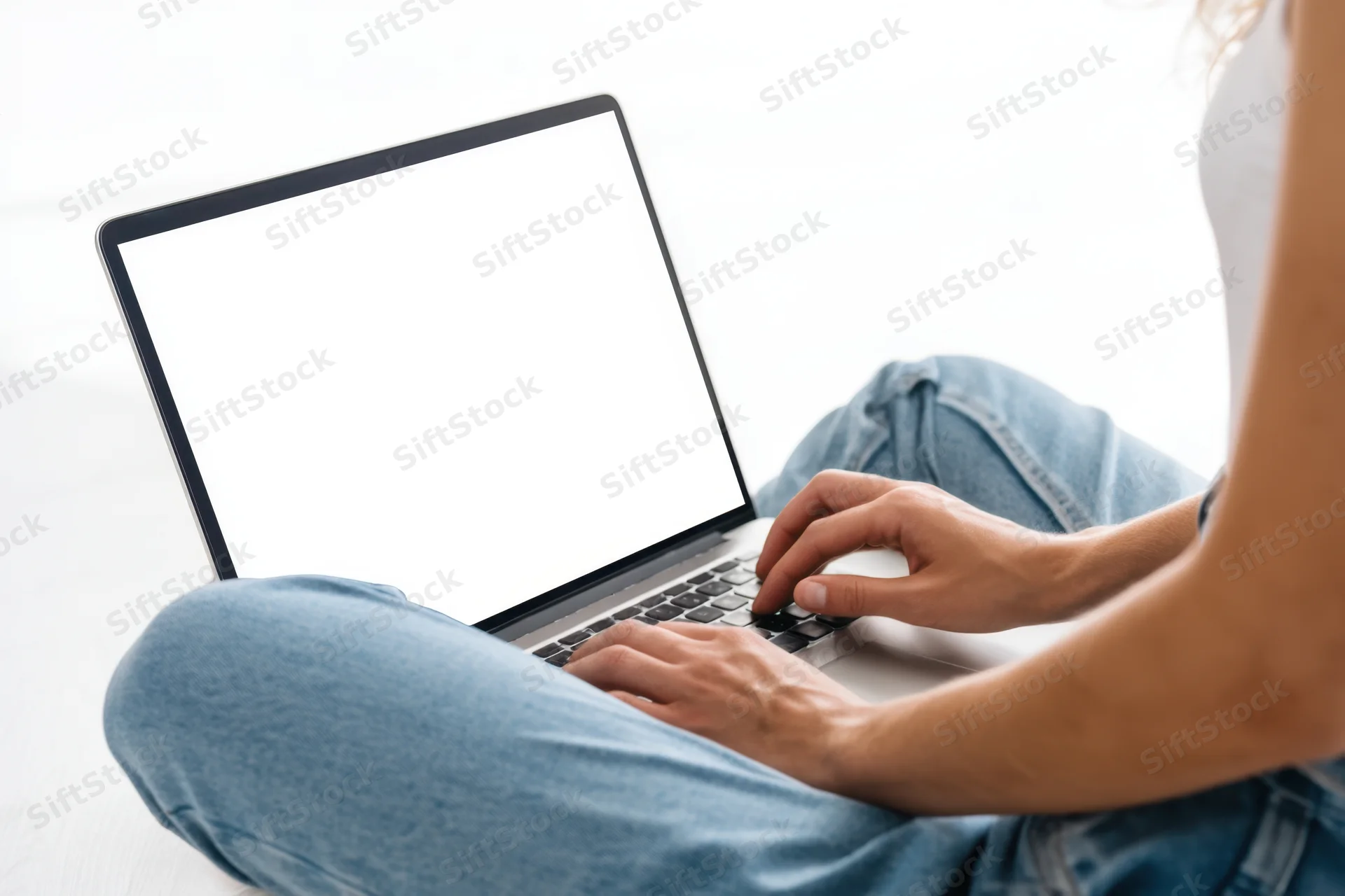 Woman typing on laptop while sitting on floor in casual jeans and white top