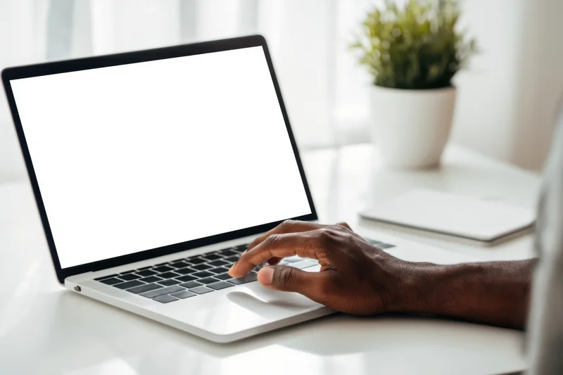 Man typing on silver laptop with blank white screen at home office desk