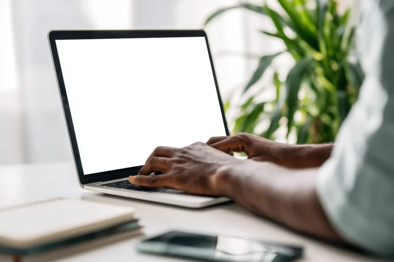 Man typing on slim laptop with blank white screen at home office desk
