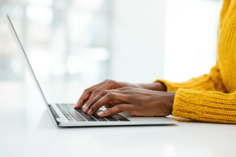 Woman typing on a slim silver laptop at a white desk in an office setting