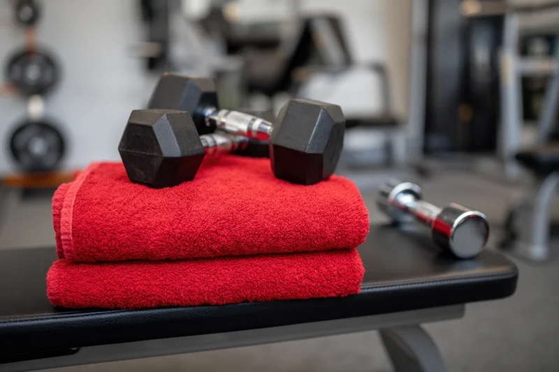 Two dumbbells resting on a stack of red towels on a gym bench