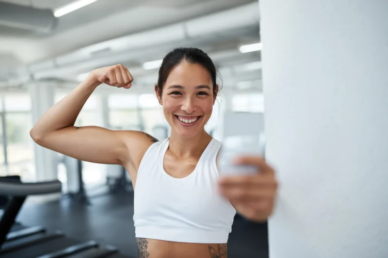 Woman flexing bicep and smiling in gym wearing white sports bra