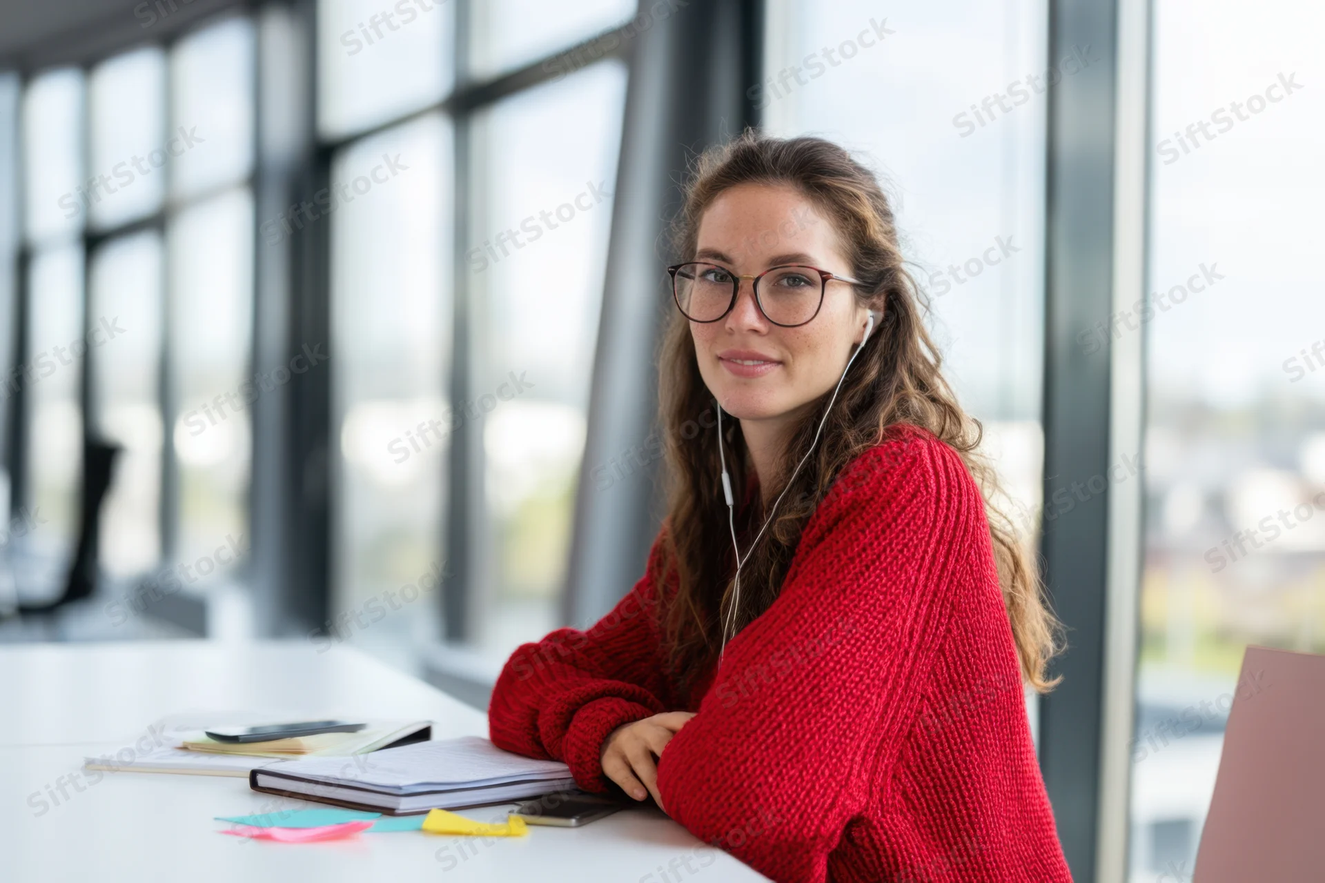 Woman in red sweater studying at white desk by large window in modern office