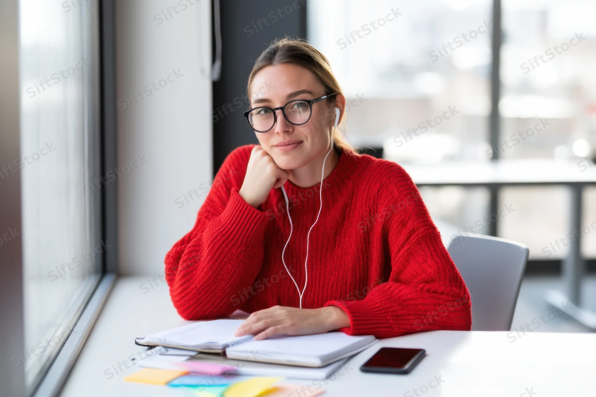 Woman in red sweater studying at white desk by large window in office
