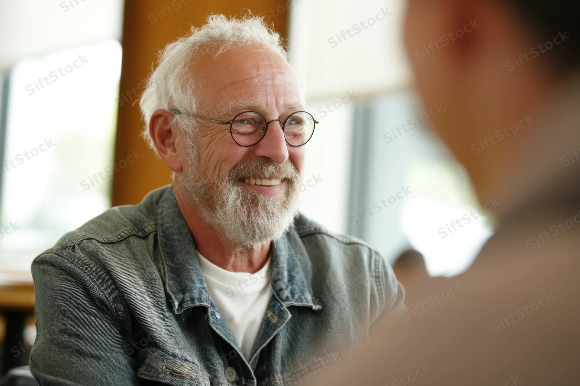 Senior man with white beard and round glasses smiling during a conversation indoors