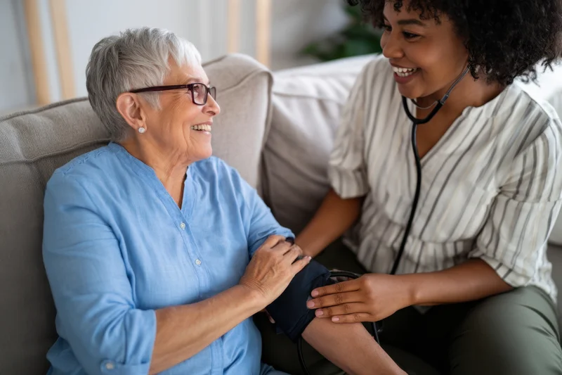 Senior woman receiving blood pressure check from nurse in home setting