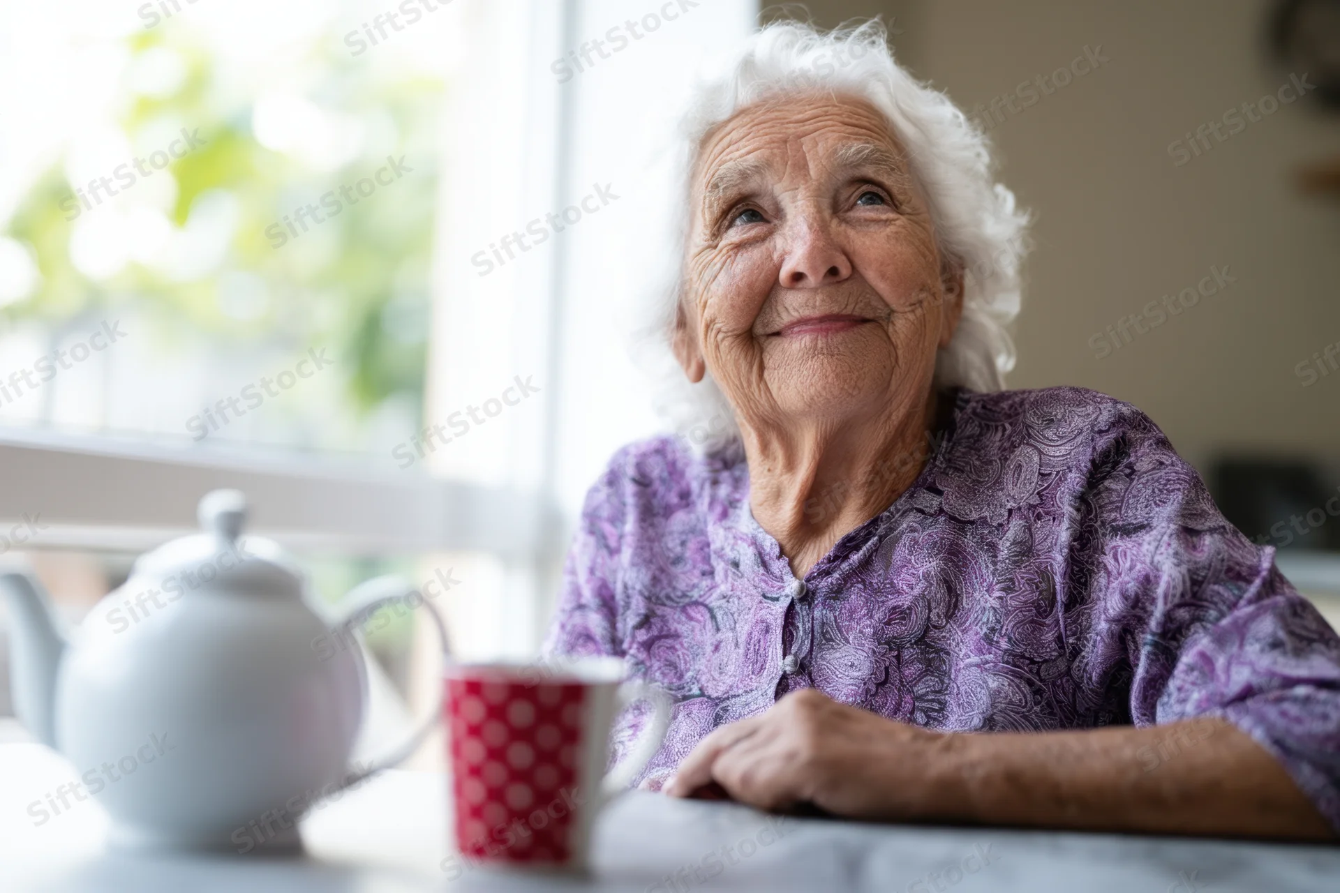 Elderly woman smiling while seated at kitchen table with tea and window view