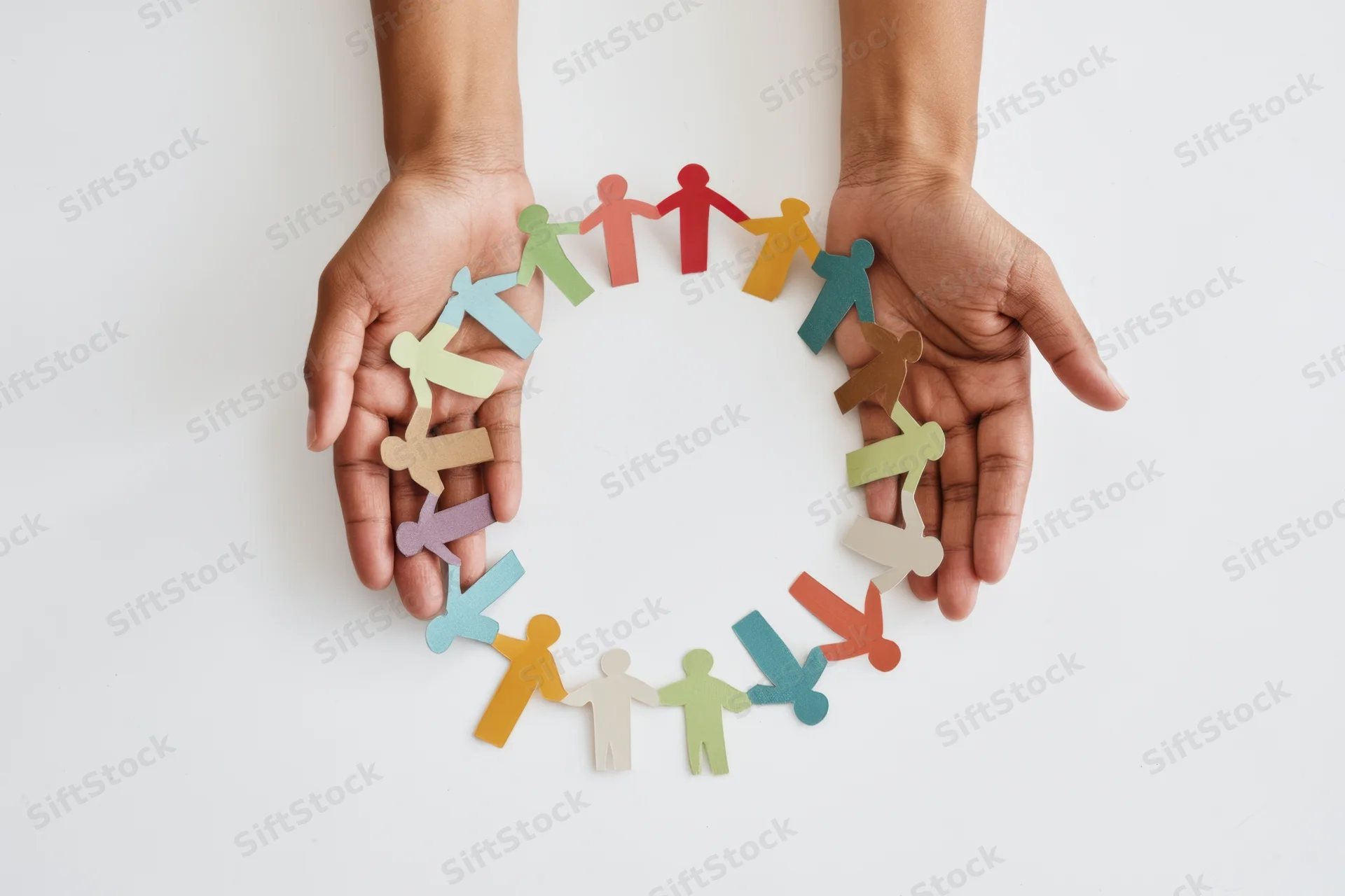 Hands cupping a circle of multicolored paper cut-out human figures on white surface