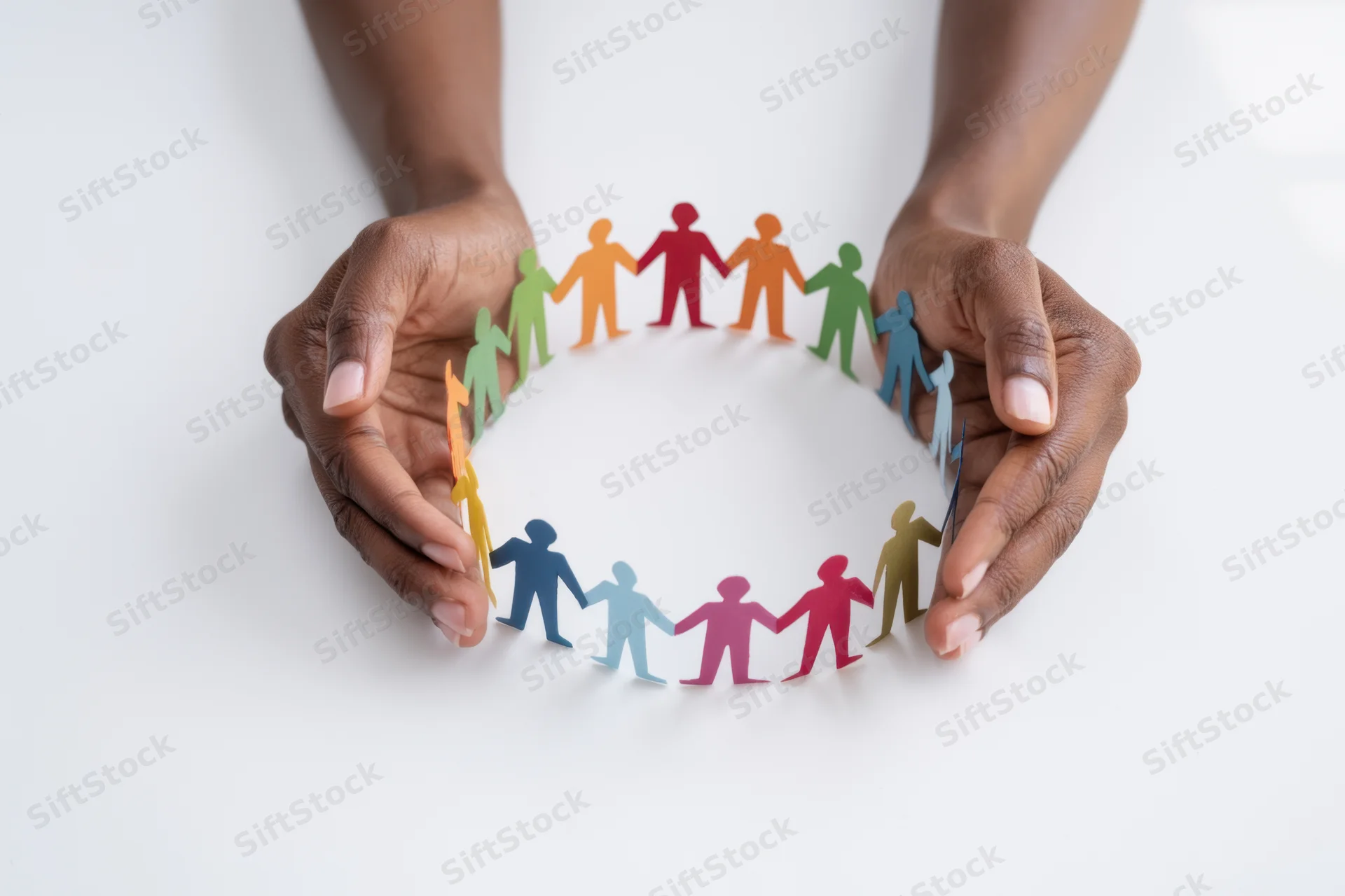 Hands cupping a circle of multicolored paper cut-out human figures on white background