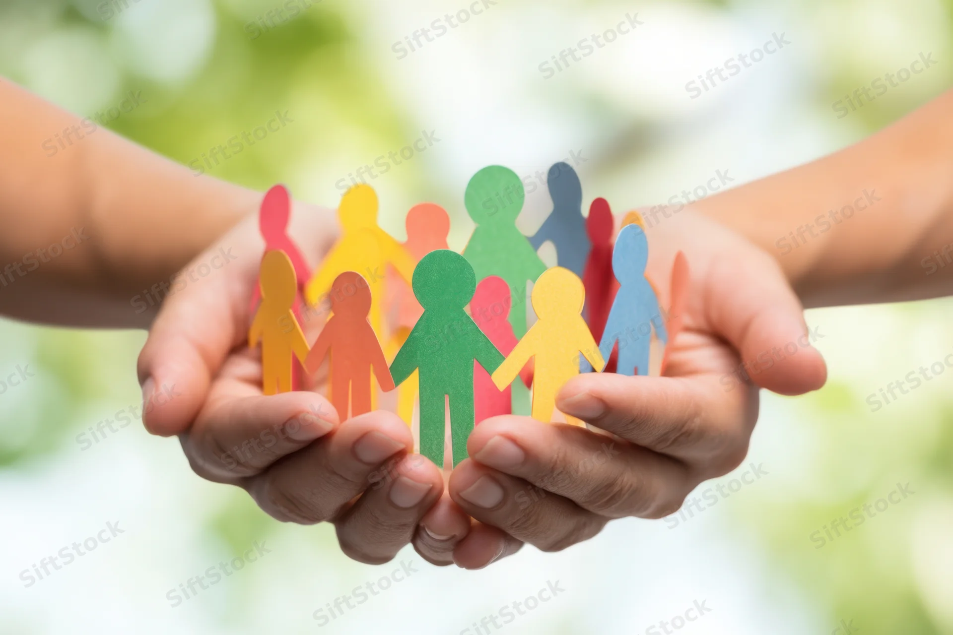 Hands cupping colorful paper cutout people in a circle, outdoors