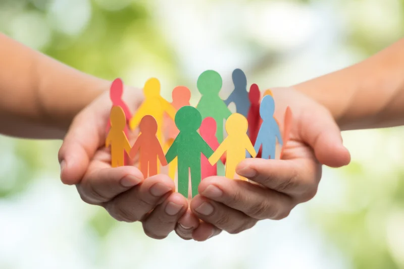 Hands cupping colorful paper cutout people in a circle, outdoors