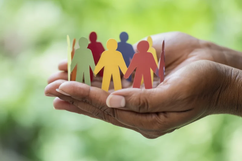Hands cupping colorful paper cutout people against a green natural background