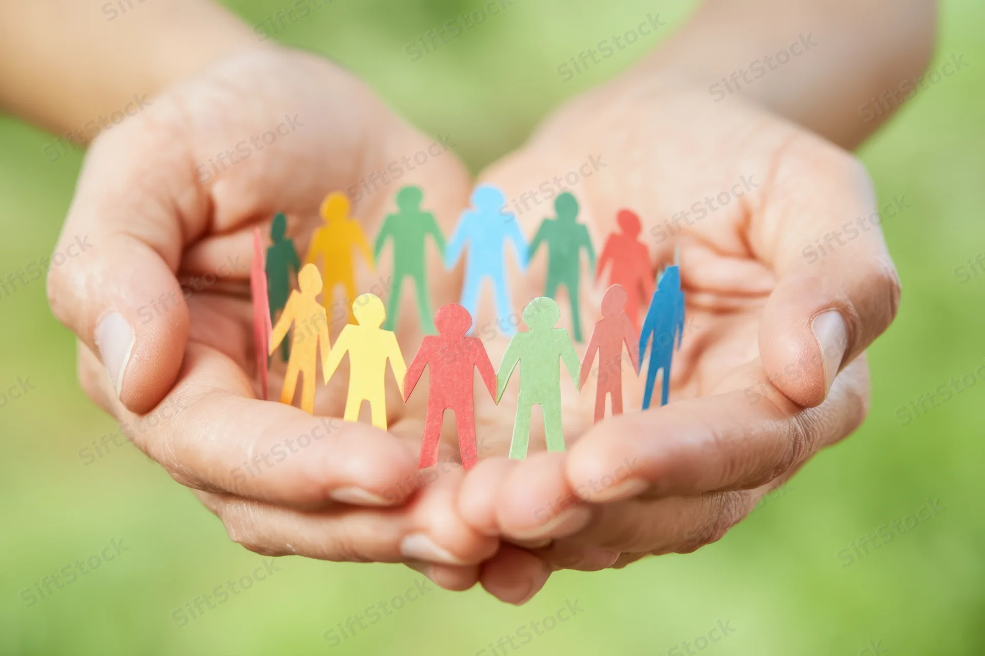 Hands cupping colorful paper cutout people against a blurred green background