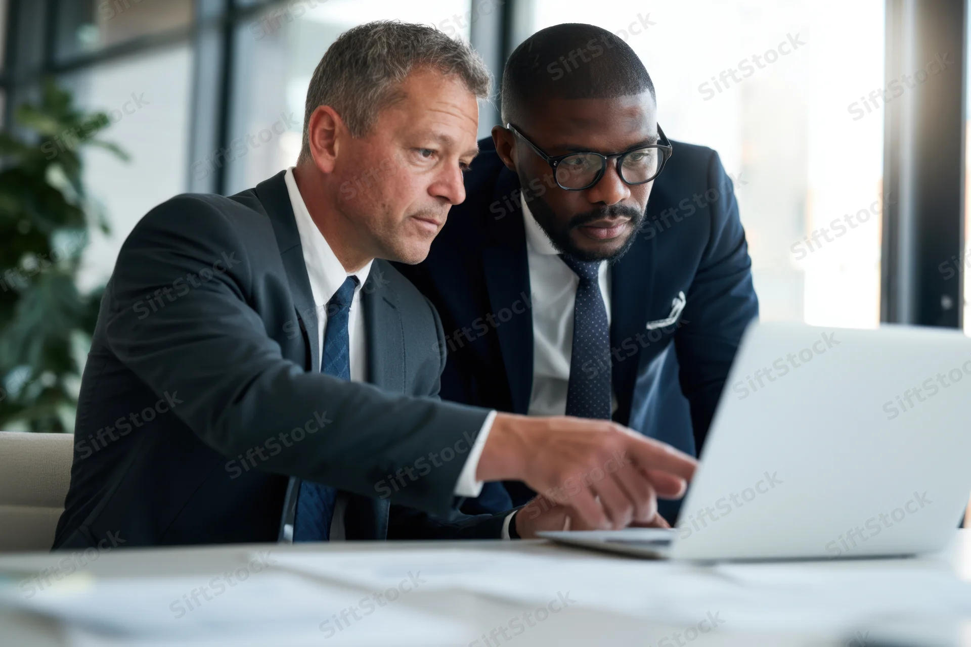 Two business professionals in a bright office reviewing content on a laptop together