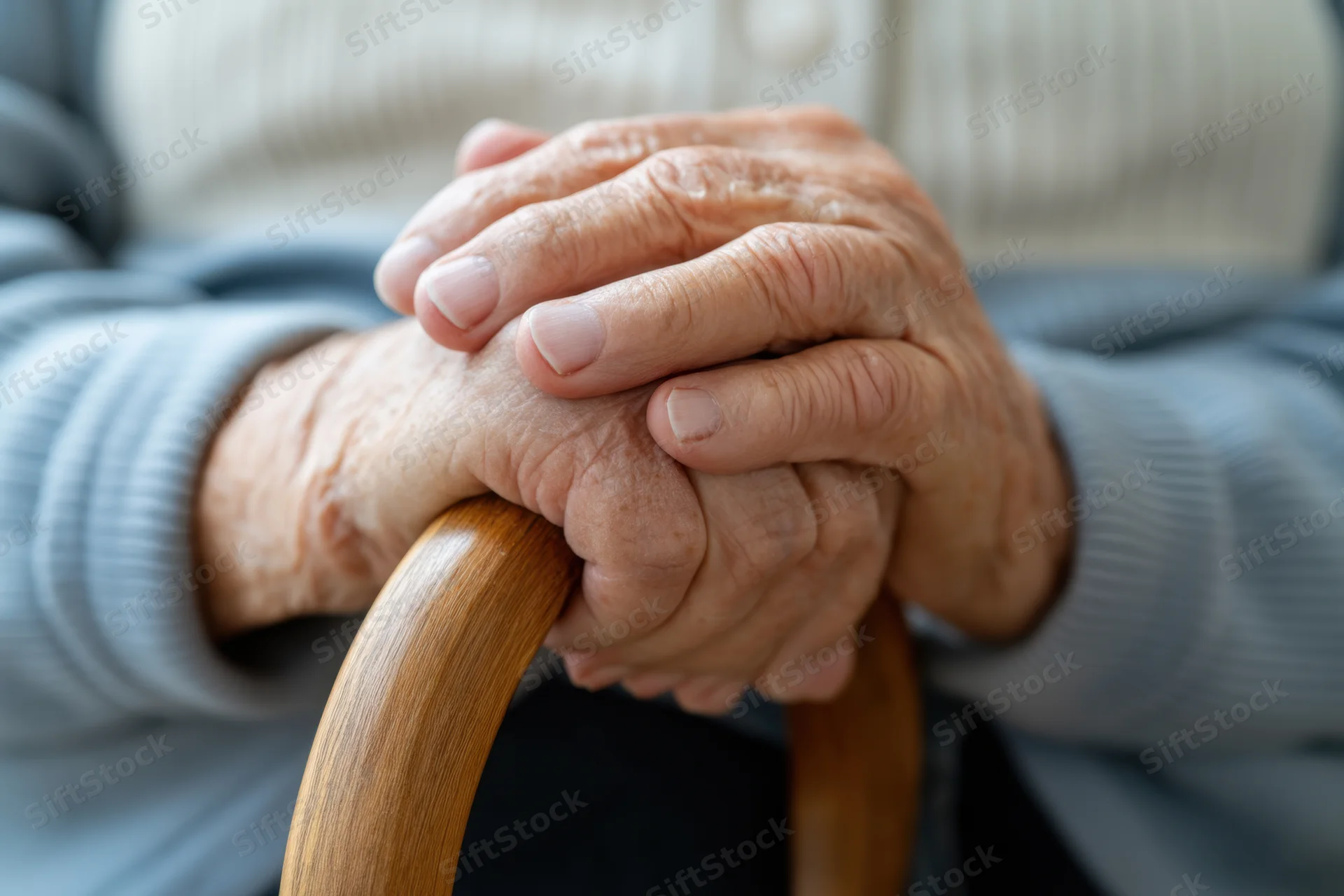 Elderly hands clasped over a curved wooden cane
