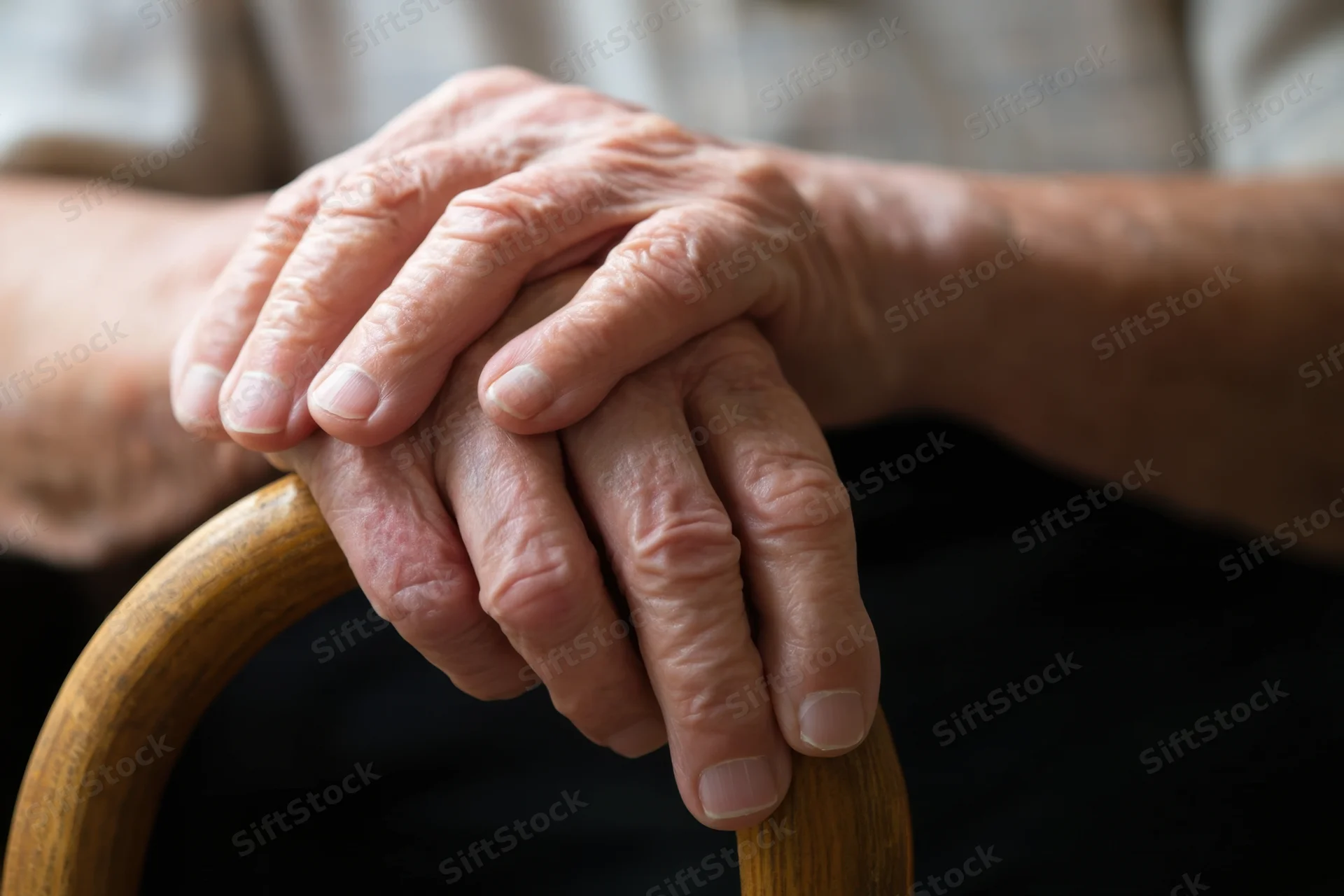 Elderly hands clasped over a curved wooden cane