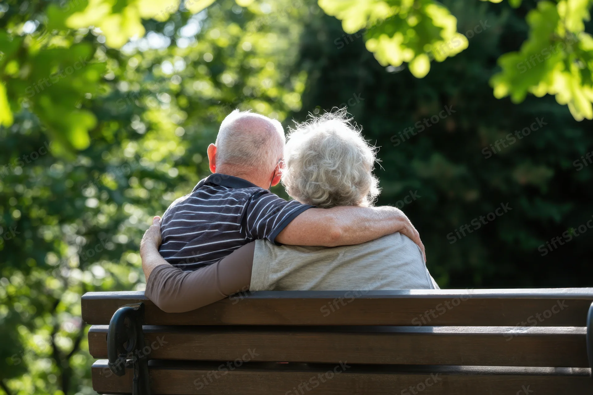 Elderly couple embracing on a wooden park bench surrounded by green trees