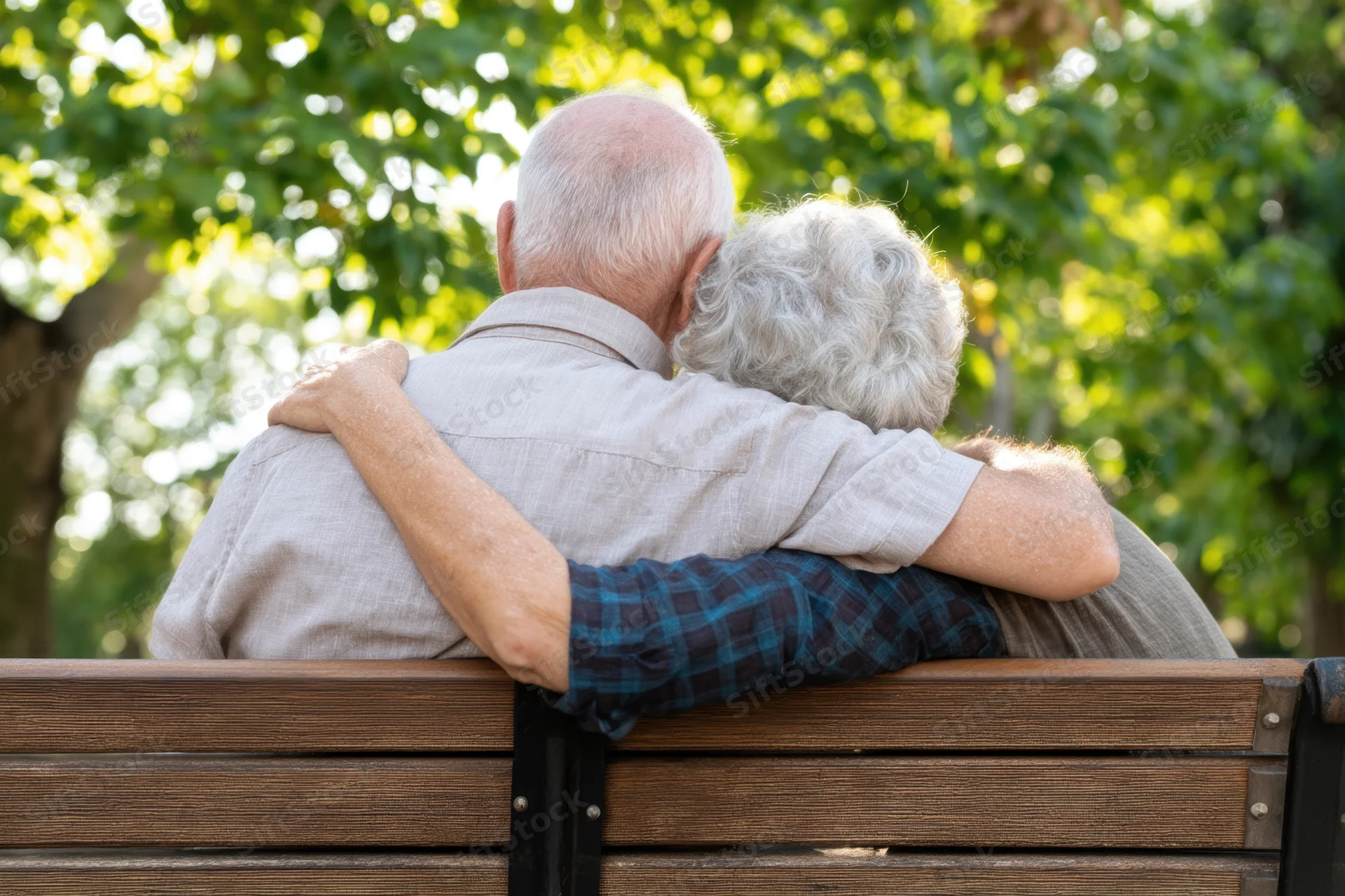 Elderly couple embracing on a wooden park bench surrounded by green trees