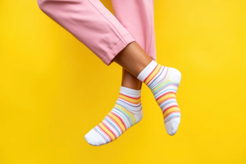 Legs crossed at ankles wearing striped pastel socks against yellow background