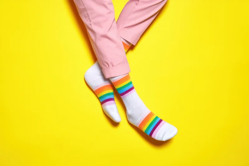 Legs crossed at ankles wearing rainbow-striped socks and pink trousers against yellow background