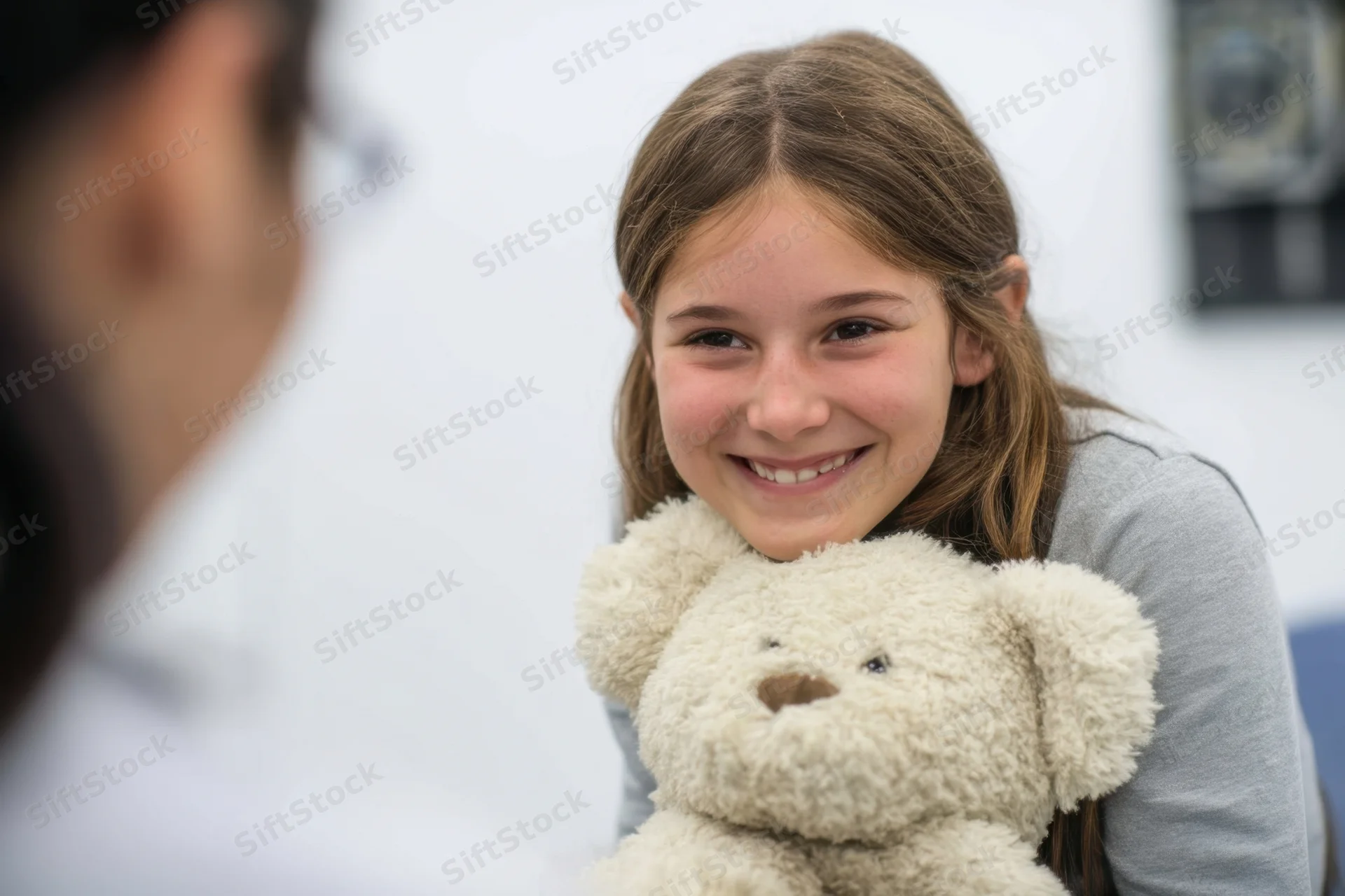 Young girl smiling while hugging a soft teddy bear in a clinic setting