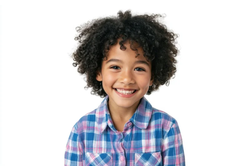 Young girl with curly black hair smiling in a blue and pink plaid shirt against a white background