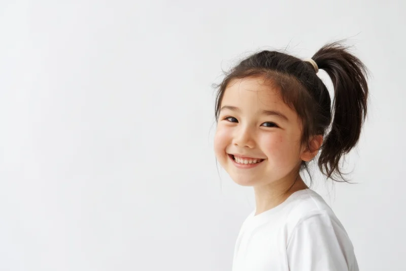 Young girl smiling with dark hair in high ponytail against white background