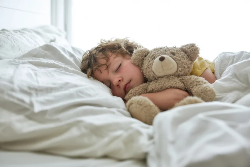 Child sleeping peacefully in bed hugging a plush teddybear