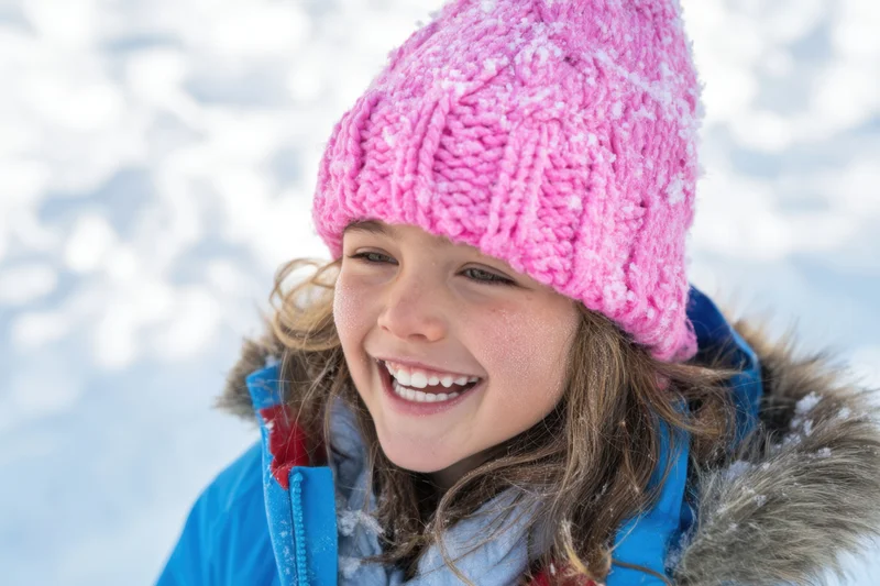 Smiling girl in pink knit hat and blue winter jacket outdoors in snow