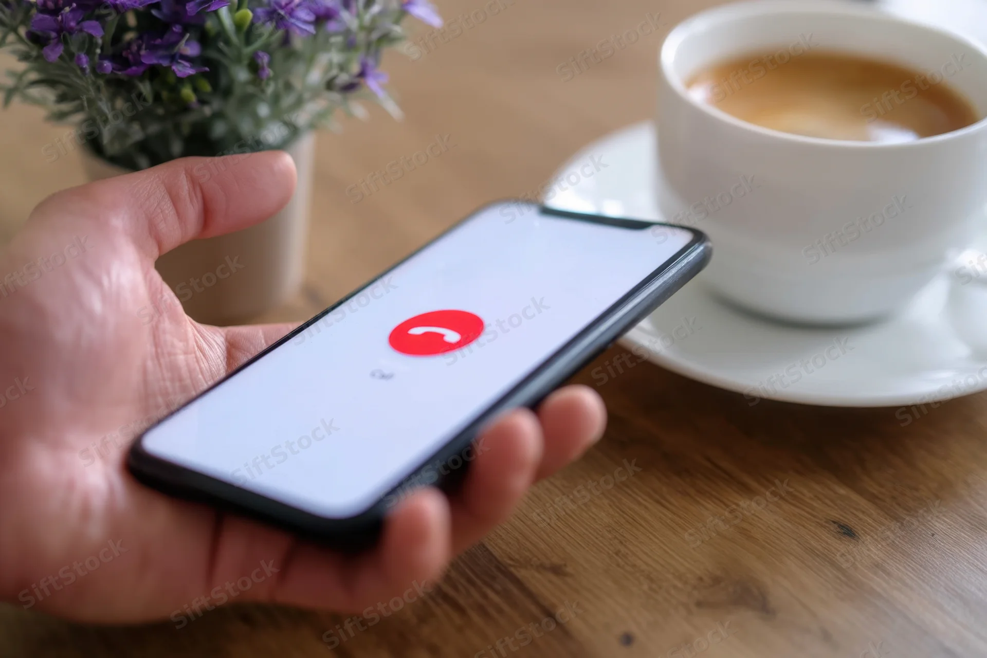Hand holding smartphone with call ending screen near coffee cup on wooden table