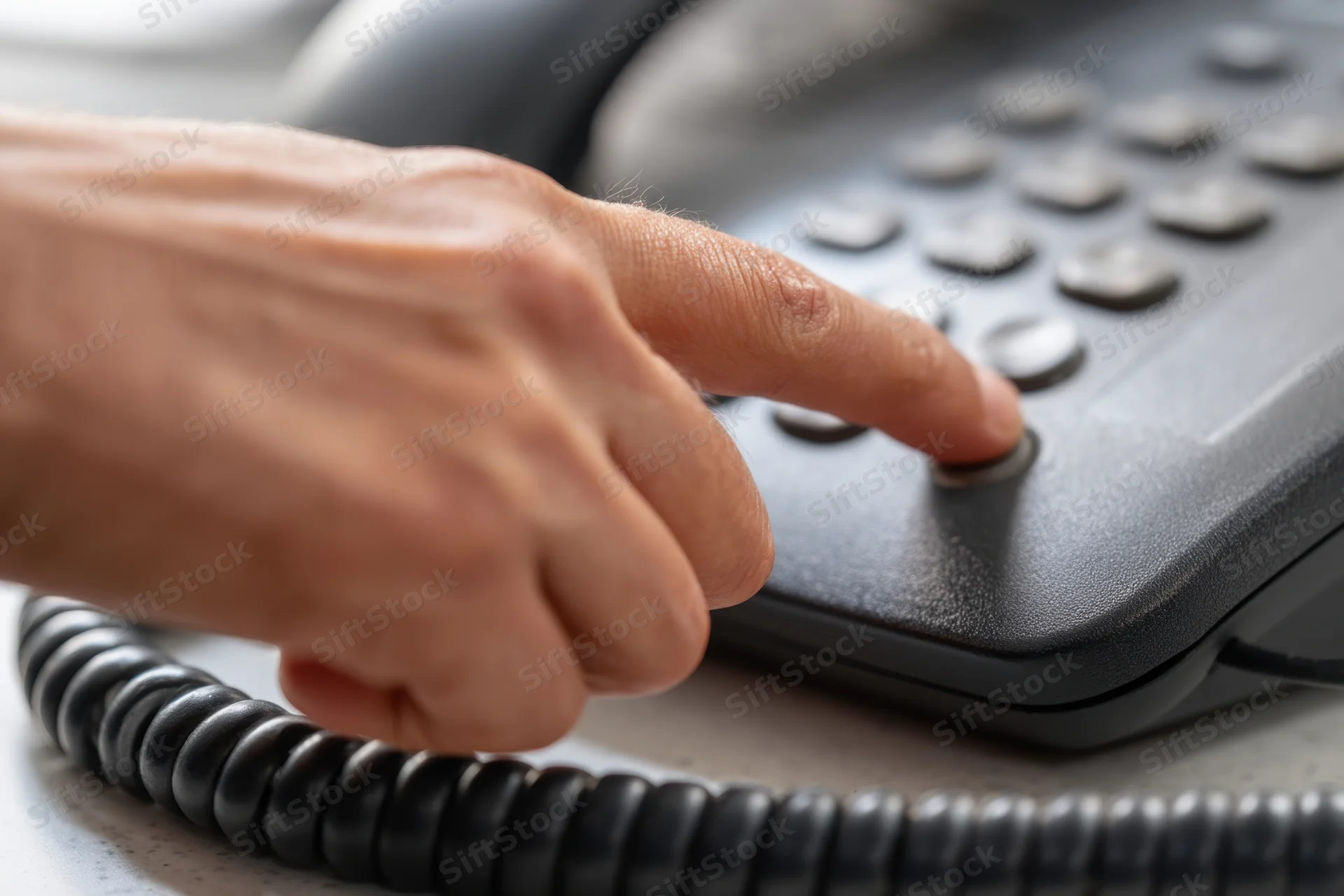 Hand pressing button on desk landline telephone
