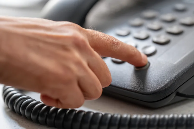 Hand pressing button on desk landline telephone