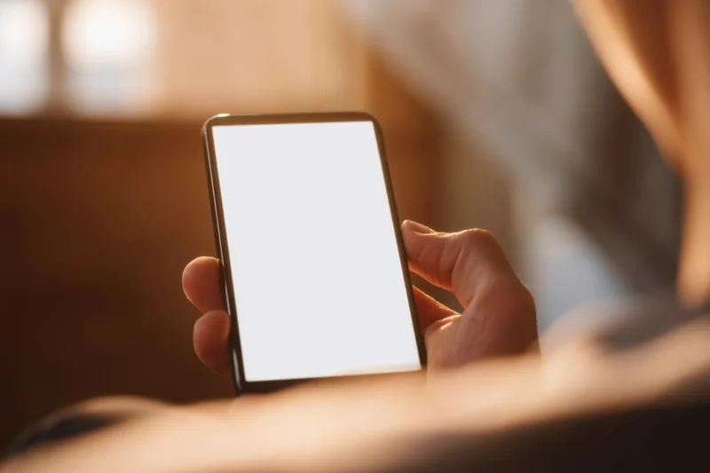 Hand holding smartphone with bright white screen in closeup view