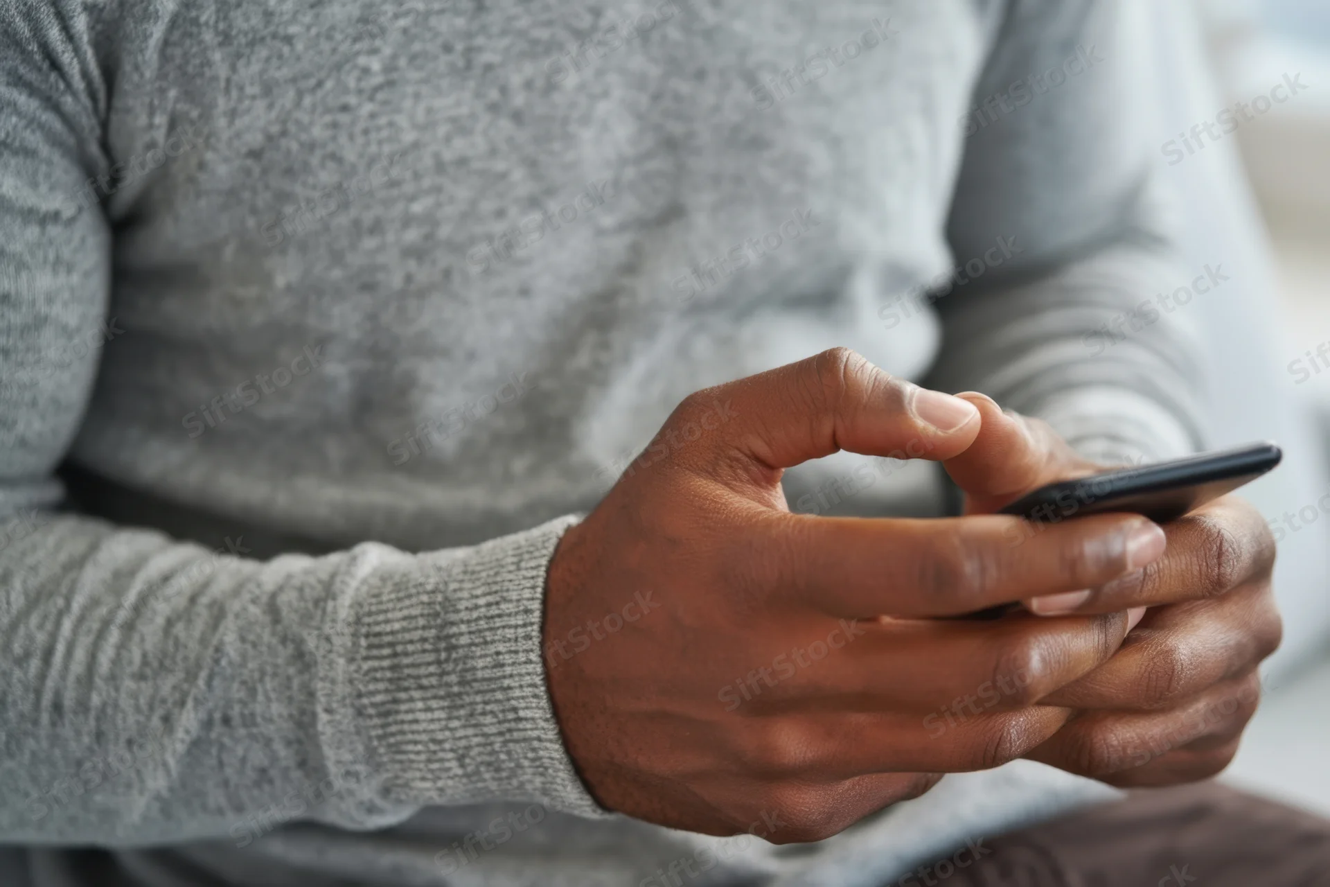 Man in gray sweater typing on smartphone indoors