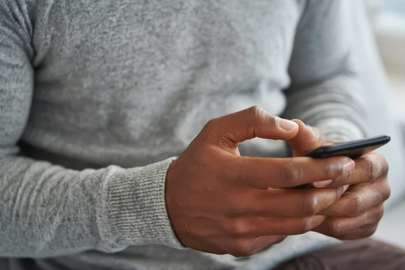 Man in gray sweater typing on smartphone indoors