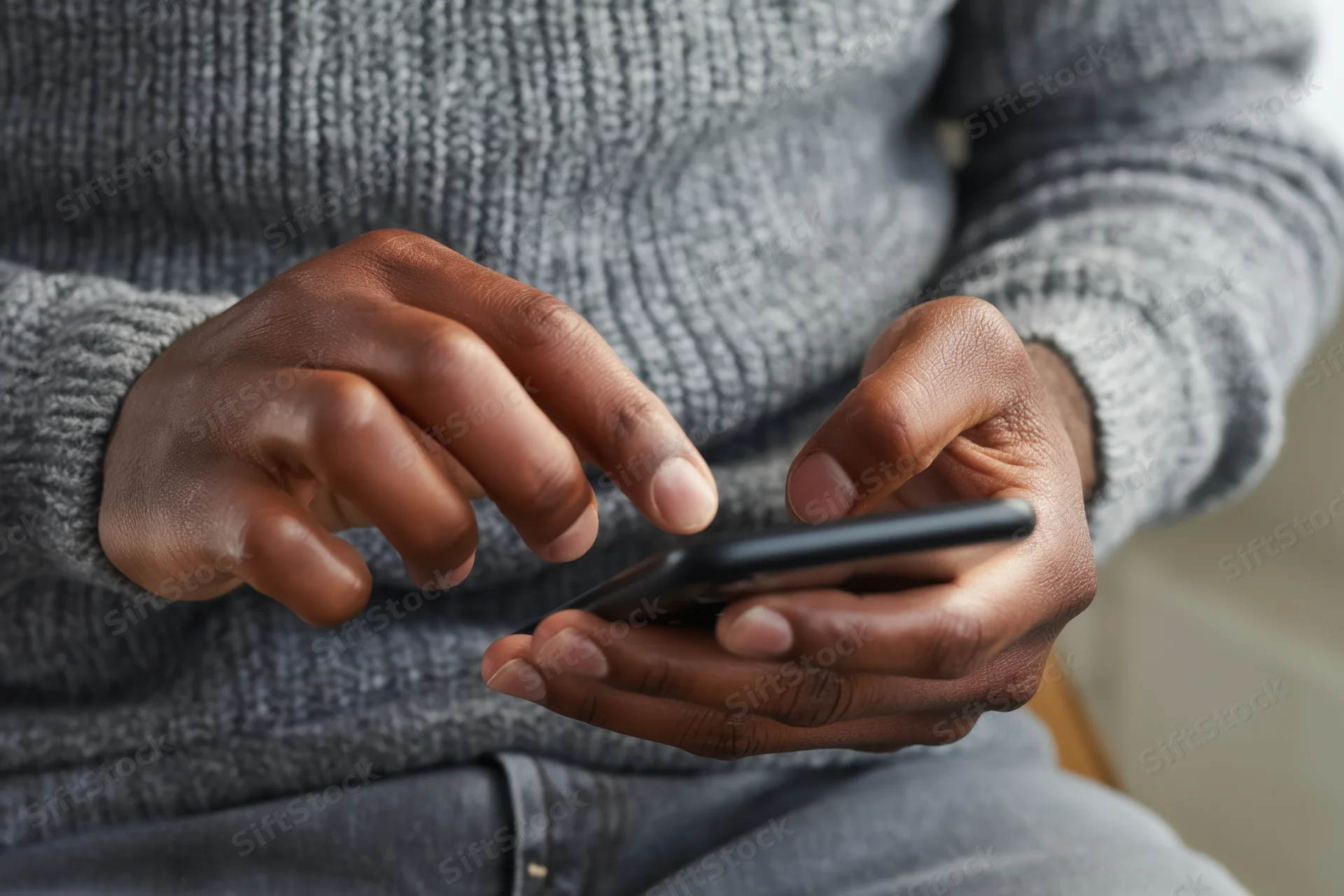 Close-up of hands typing on a smartphone while seated indoors