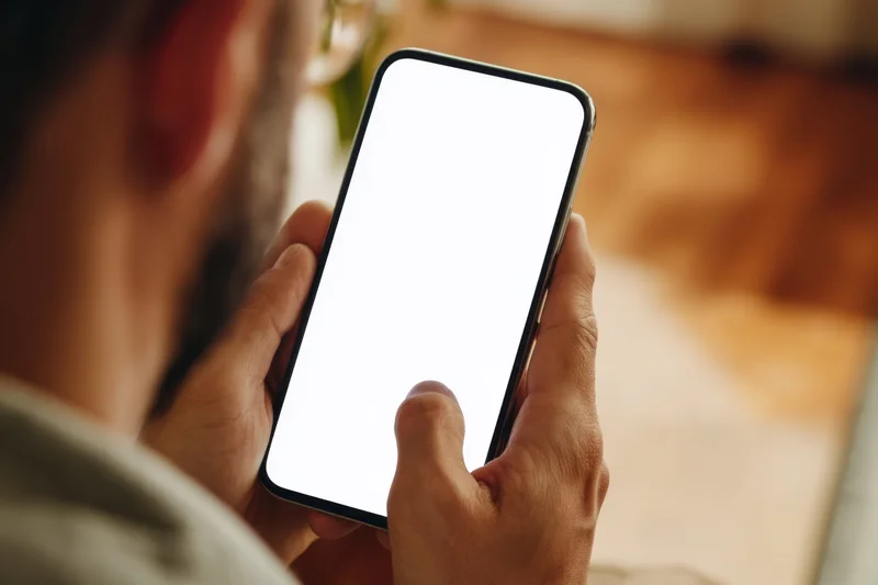Man holding smartphone with blank white screen from behind in indoor setting