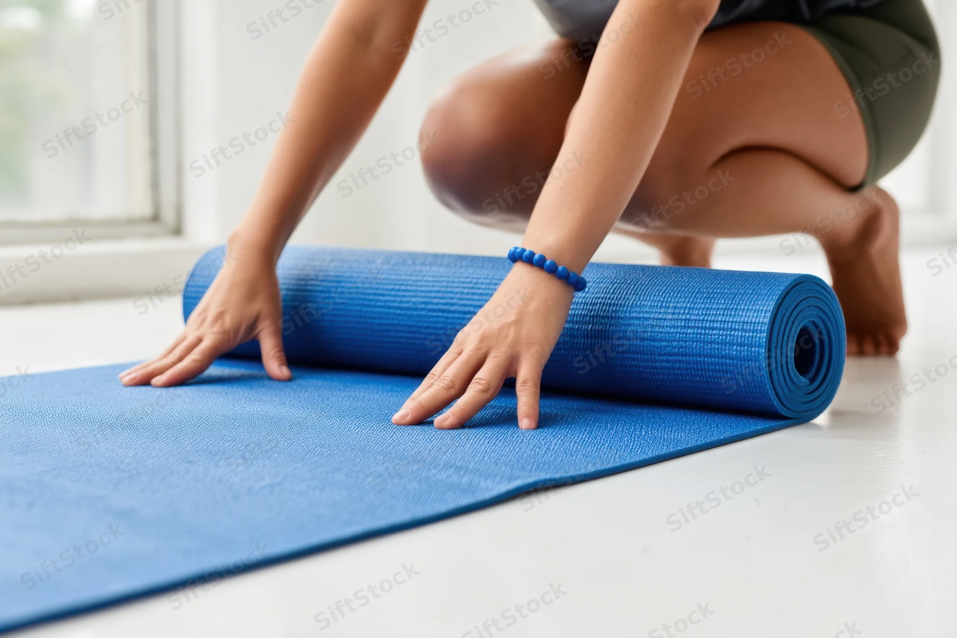 Woman unrolling a blue yoga mat on a bright indoor floor