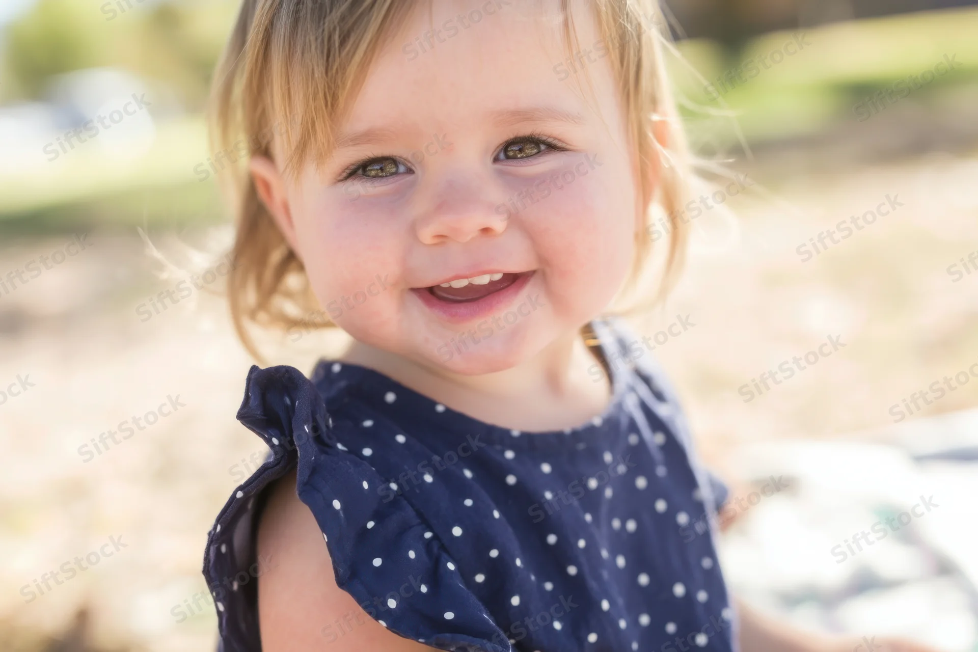 Smiling toddler in navy polka dot dress outdoors in sunlight