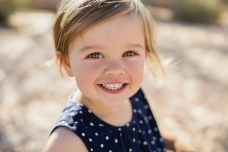 Smiling toddler girl in navy polka dot dress outdoors in sunlight