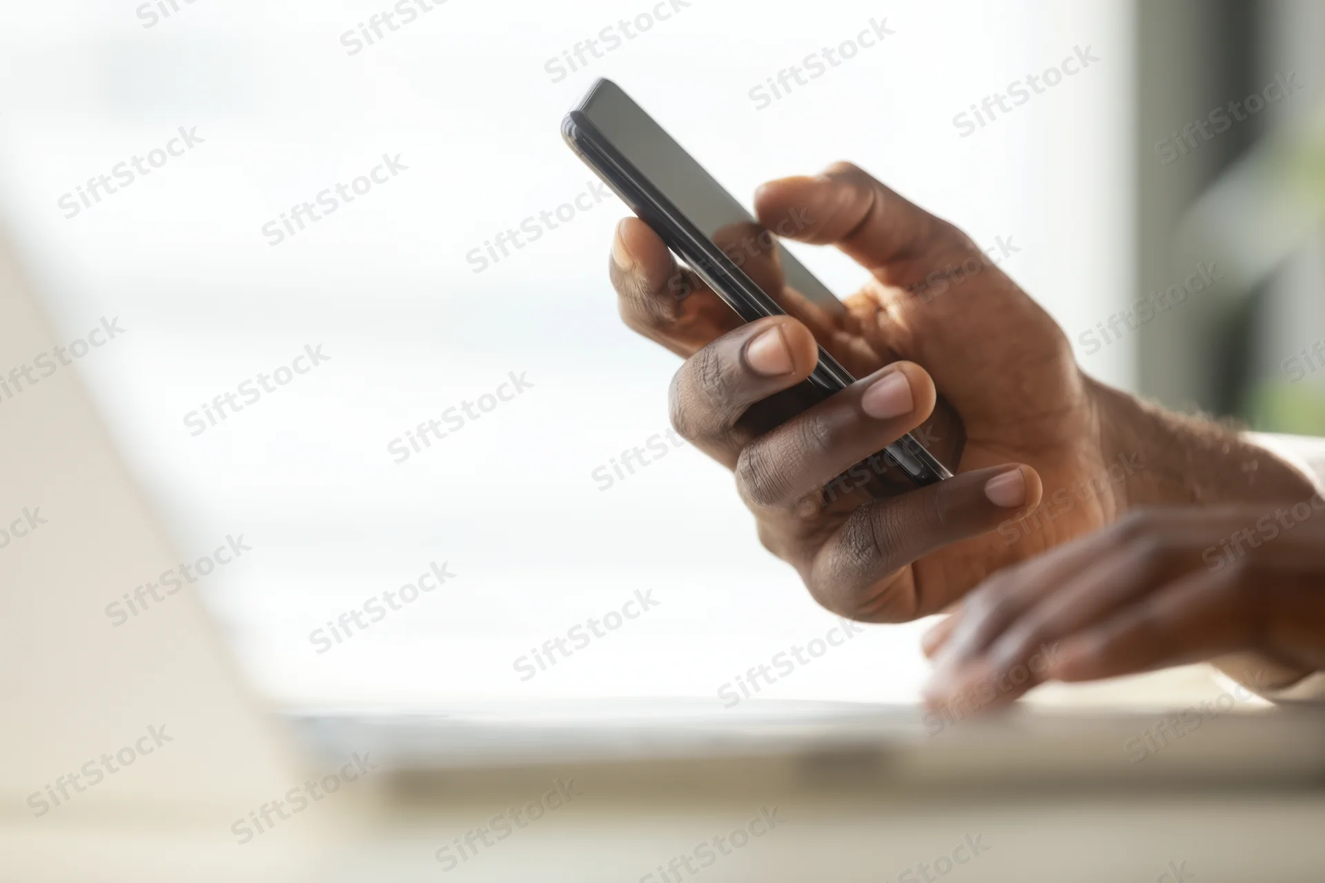 Hands holding smartphone above laptop on desk