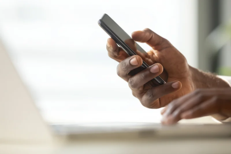 Hands holding smartphone above laptop on desk