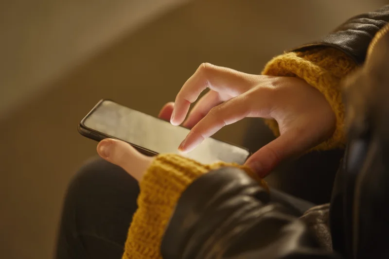 Woman’s hands holding smartphone with fingers poised over touchscreen indoors