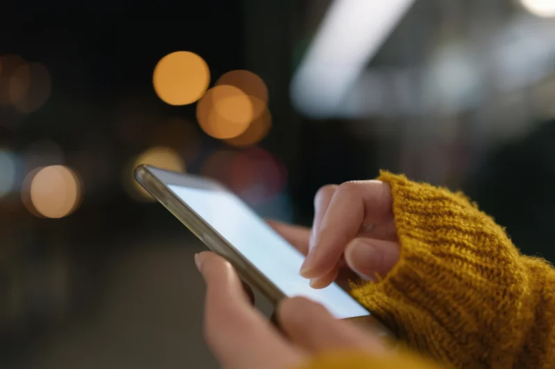 Hands holding a smartphone with screen glow in a blurred city night setting