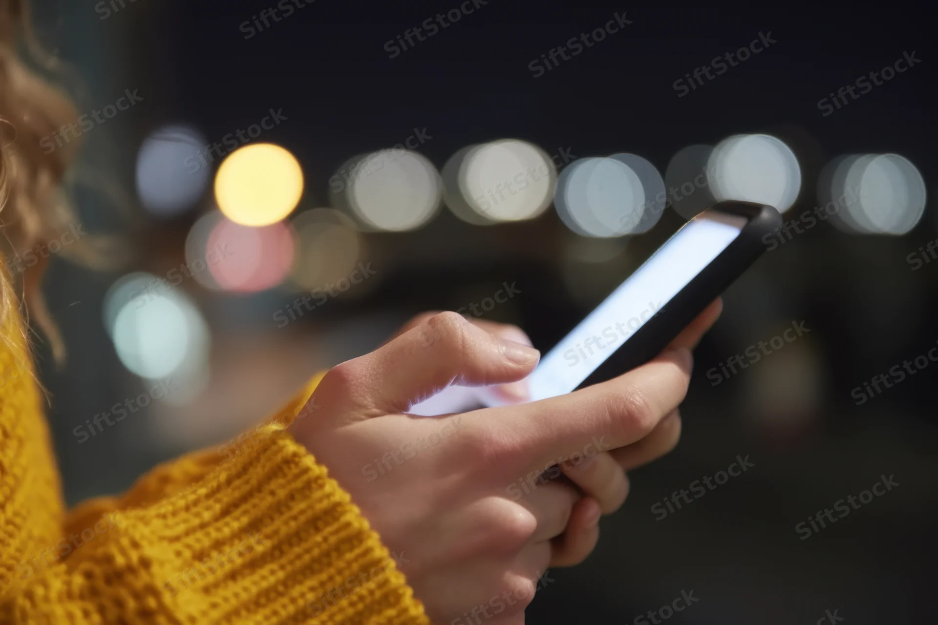 Woman holding smartphone with glowing screen at night in city setting