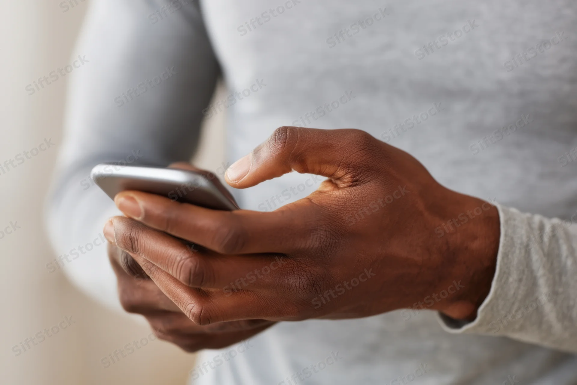 Close-up of hands tapping a smartphone while wearing a gray sweater