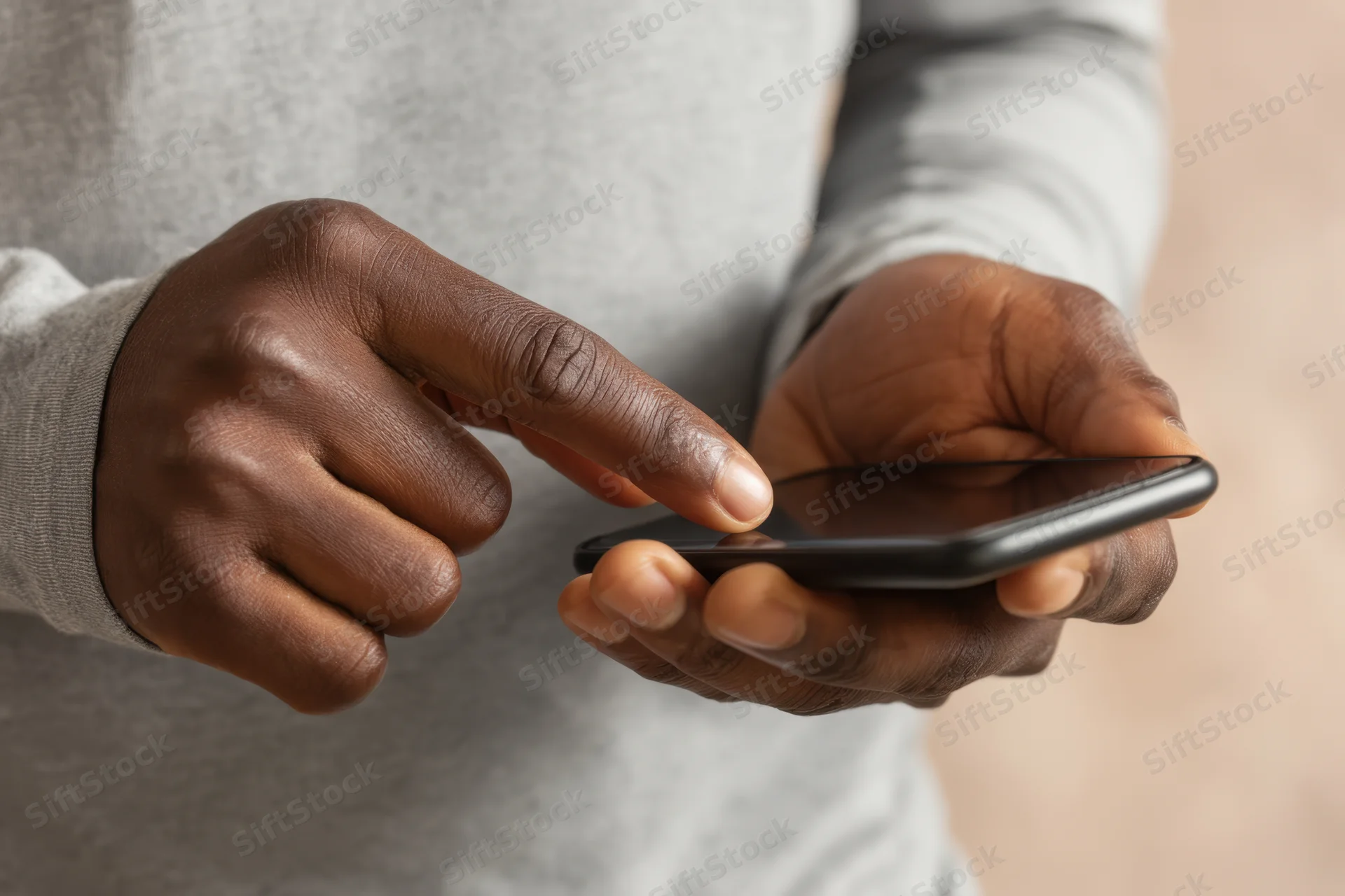 Close-up of hands tapping a smartphone while holding it in a gray sweater